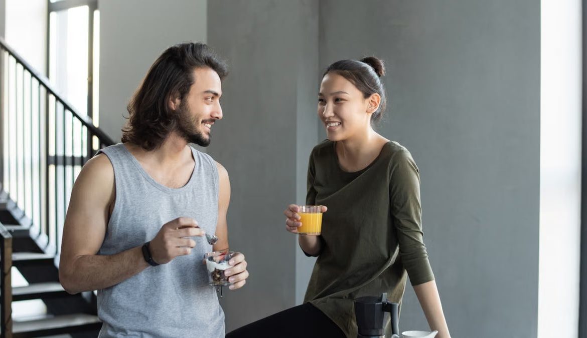 A happy young couple sharing a breakfast moment with juice and snacks indoors.