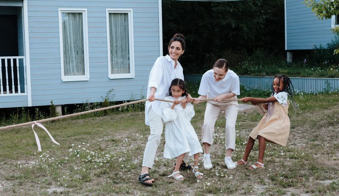 A happy family enjoys a game of tug of war in a grassy field by a house.